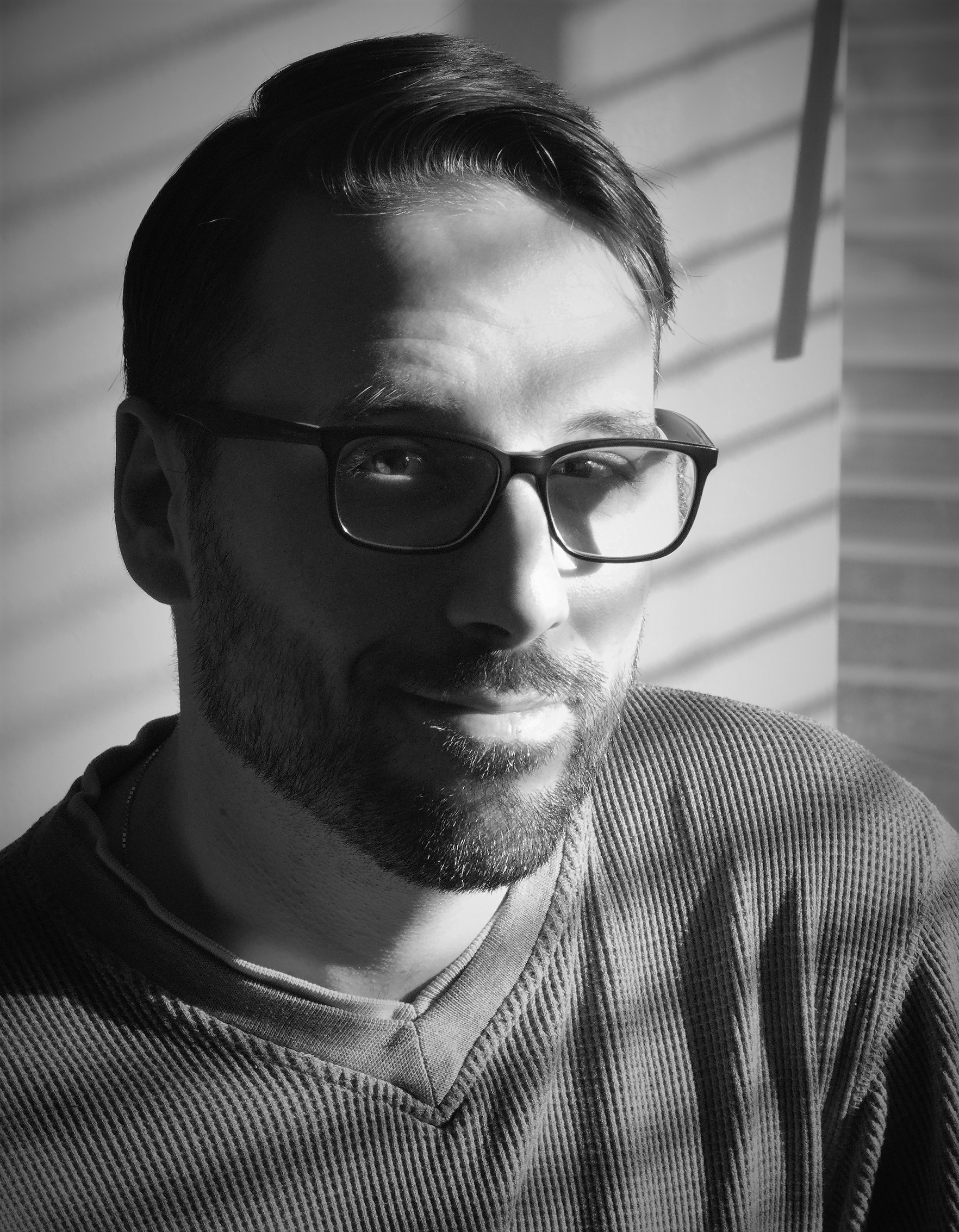 a closeup black and white image of Gregory, he is bearded and wearing rectangular glasses