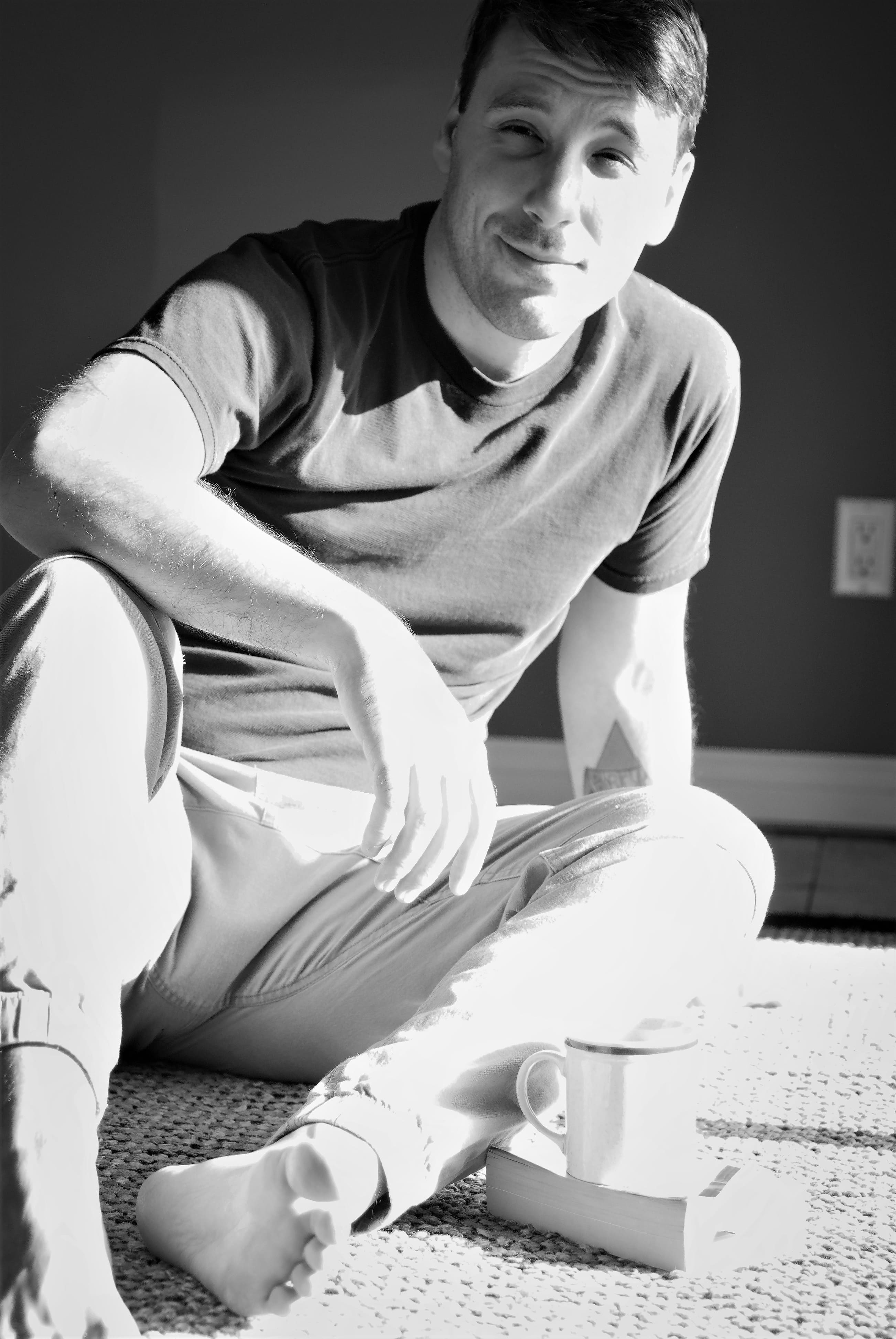 young man sitting on the floor in the sun, he is resting an arm on his knee in a relaxed way